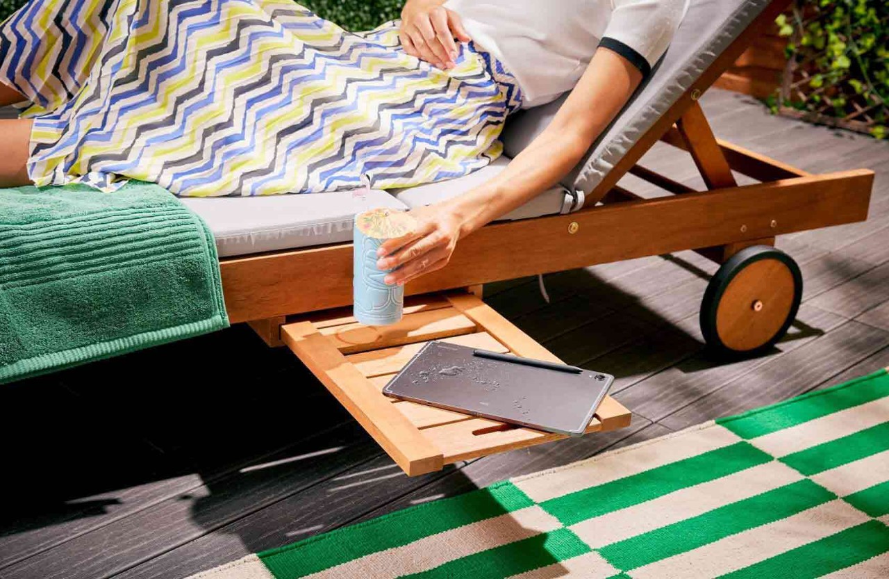 person sitting on sunlounger with a drink being placed down with liquid spilt on tablet