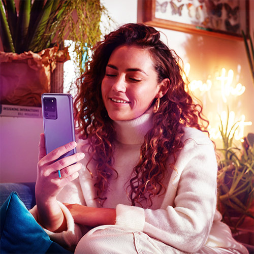 Woman holding Samsung Galaxy S20 Ultra with plants and neon sign in the background.